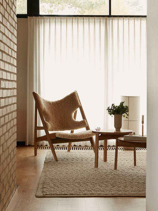 A living room with the Knitting Chair in sheepskin on a Gravel Rug, next to a Passage Lounge Table and Hashira Floor Lamp.