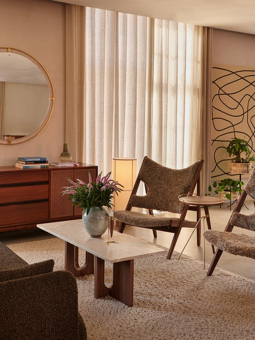 A pair of Knitting Lounge Chairs with brown sheepskin upholstery in a warm, modern living room with a marble coffee table.