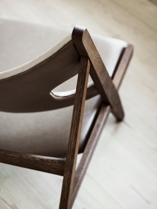 A close-up view of the Knitting Lounge Chair's dark stained oak frame and light leather back, highlighting the elbow cut-out.