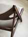 A close-up view of the Knitting Lounge Chair's dark stained oak frame and light leather back, highlighting the elbow cut-out.
