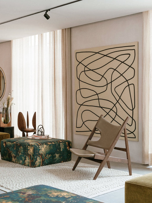 The Knitting Lounge Chair in natural oak and light leather, pictured in a bright, modern living room with abstract wall art.
