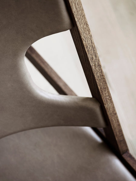 A detailed close-up of the Knitting Lounge Chair, showing the grain of the dark oak frame against the soft, taupe leather.