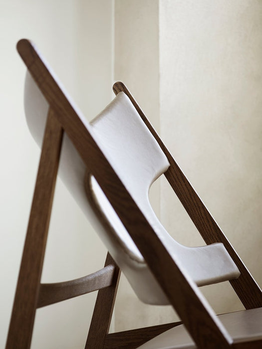 A close-up of the Knitting Lounge Chair, showing the elegant curve of the dark wood frame against the light leather seat.