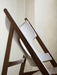A close-up of the Knitting Lounge Chair, showing the elegant curve of the dark wood frame against the light leather seat.