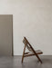 Side view of the Knitting Lounge Chair with a dark oak frame and light leather upholstery, against a textured off-white wall.