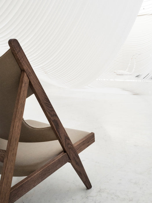 Close-up of the dark wood frame of the Knitting Lounge Chair with light upholstery, set in a minimalist white space.