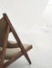 Close-up of the dark wood frame of the Knitting Lounge Chair with light upholstery, set in a minimalist white space.