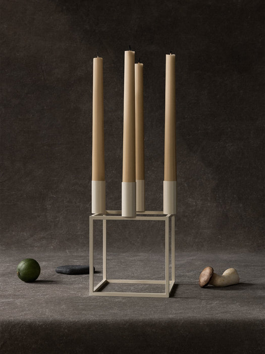 The ivory Kubus 4 candle holder with four tall beige candles, styled on a dark textured surface with a lime and a mushroom.