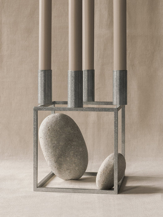 The Kubus 4 zinc candle holder with four taupe candles is styled with two smooth grey stones placed inside its square frame.