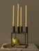 The olive-coloured Kubus 4 candle holder holds four tall cream candles. A green pear is resting inside its geometric base.