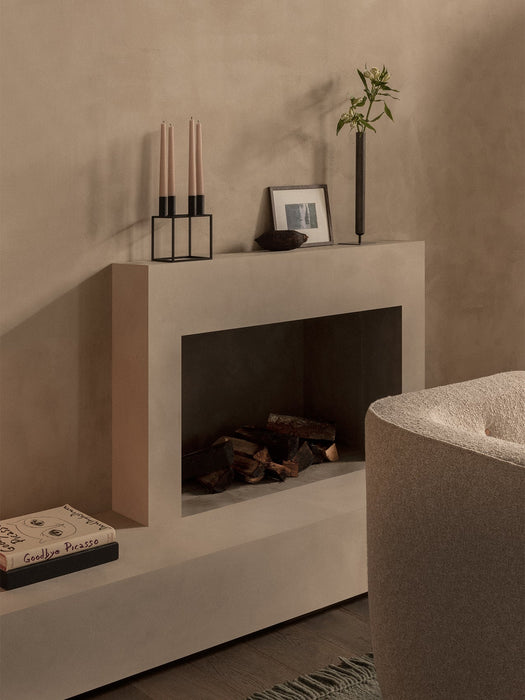 A black Kubus 4 Candle Holder with beige candles and a dark Stance Vase with flowers sit on a modern fireplace mantel.