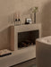 A black Kubus 4 Candle Holder with beige candles and a dark Stance Vase with flowers sit on a modern fireplace mantel.