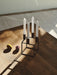 Black by Lassen Kubus 4 candle holder with four white candles on a sunlit dark wood table next to two paper ornaments.