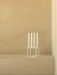 A white, geometric Kubus Candle Holder holding four tall white candles on a beige surface against a matching beige wall.