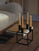 A black Kubus 4 candle holder with four beige candles, styled on books on a wooden Jager Lounge Table with a Tired Man chair.