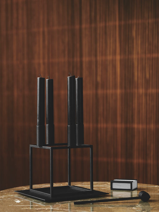 Black Kubus 4 candle holder with four black candles on a Kubus Base, with a Matchbox Cover and Snuffer on a marble tabletop.