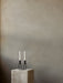 A black Kubus Line Candle Holder with two white candles on a marble Plinth Pedestal against a muted, textured beige wall.