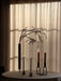 A still life with a Stance Vase holding a branch and lit candles in Kubus Line and Kubus Mikro holders on a softly lit table.