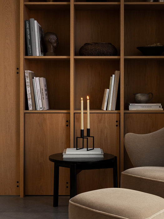 Kubus Line candlestick on a side table beside an Ingeborg Lounge Chair and Footstool, in front of a large wooden bookcase.