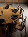 High-angle view of four oak Merkur Dining Chairs with armrests surrounding a round oak Androgyne Dining Table set for a meal.