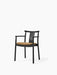 A Merkur Dining Chair with Armrests in black oak, shown from an angle. The chair has a textured, light brown bouclé seat.