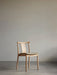 The Merkur Dining Chair in natural oak with a green fabric upholstered seat, shown front-on against a plain grey wall.