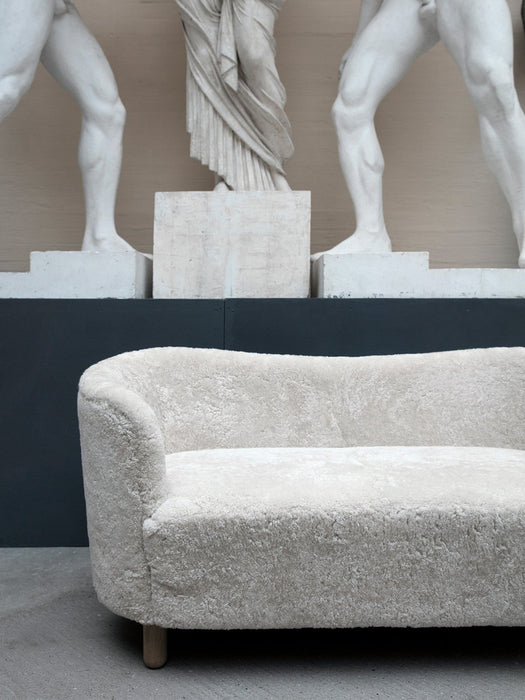 The Mingle Sofa in off-white Sheepskin on a concrete floor, set against a dark wall with classical white statues.