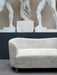 The Mingle Sofa in off-white Sheepskin on a concrete floor, set against a dark wall with classical white statues.
