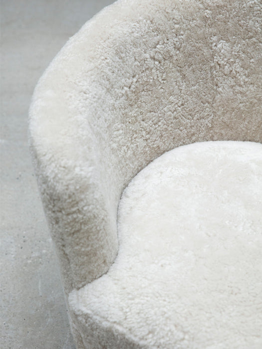 A close-up shot of the Mingle Sofa, highlighting the plush, textured off-white sheepskin covering the curved seat and back.