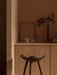 A dark wood ML 42 Counter Stool in a warm, minimalist kitchen. On the counter are a Stance Vase, Triptych Bowl, and glass.