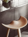 Close-up of the ML 42 Bar Stool in light wood, showcasing the sculpted seat against a dark kitchen counter with a marble top.