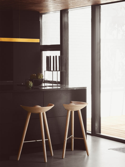 Two light oak ML 42 Counter Stools sit at a dark kitchen island. On the counter is a Kubus 8 candelabra and Kubus Bowl.