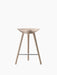 A front-on shot of the ML 42 Counter Stool in light oak, with a sculpted seat, three legs, and a steel footrest.
