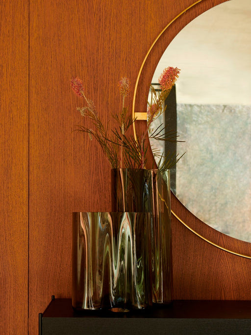 Nimbus Mirror, a round brass-framed mirror on a wood wall, styled with two dark glass vases holding flowers.