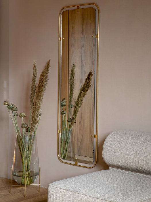 The brass-framed Nimbus Mirror on a beige wall, beside an Echasse Vase with dried botanicals and the Eave Modular Sofa.