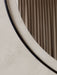 A close-up of the Nimbus Mirror, showing its slim, dark frame against a textured off-white wall, reflecting a soft curtain.