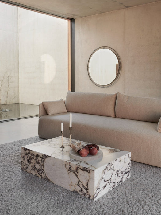A modern living room with a beige Offset Sofa, a marble Plinth coffee table, and a round Nimbus Mirror on a concrete wall.