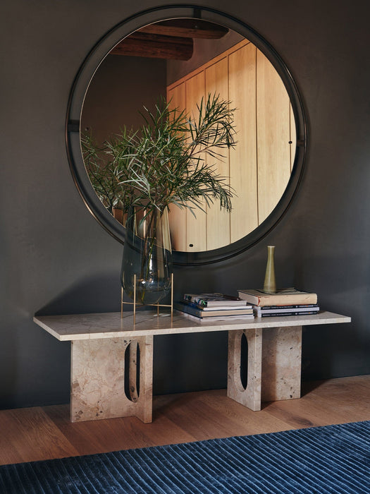 The Androgyne Lounge Table in marble, styled with a vase of foliage and books, sitting below a large circular mirror.