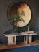 The Androgyne Lounge Table in marble, styled with a vase of foliage and books, sitting below a large circular mirror.