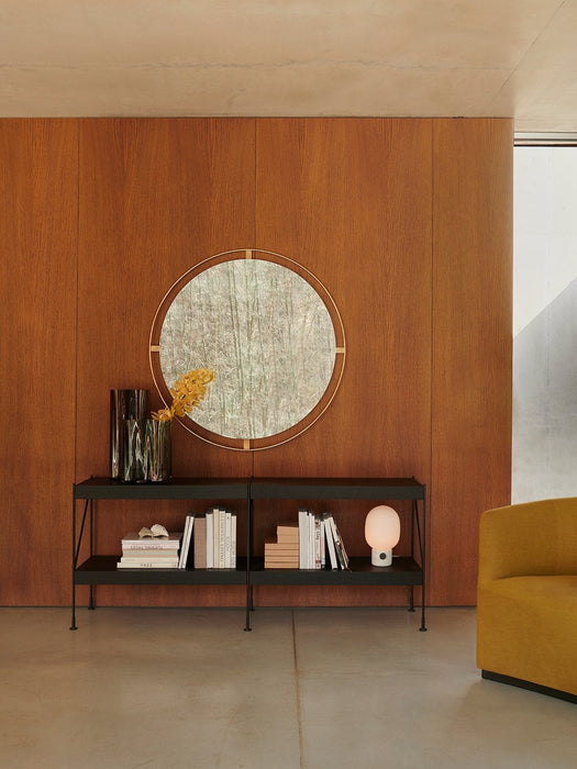 A lifestyle setting showing a Nimbus Mirror on a wood-panelled wall, above a black Zet Shelf with a JWDA Lamp and Aer Vase.