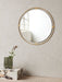 The round Nimbus Mirror in a brass frame hangs on a grey wall above a marble Plinth holding a grey Aer Vase with a flower.
