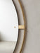 Close-up of the round Nimbus Mirror, highlighting the polished brass frame and mounting bracket against a light grey wall.
