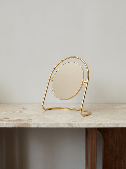 The Nimbus Table Mirror, featuring a circular mirror in a polished brass stand, rests on a veined marble tabletop.