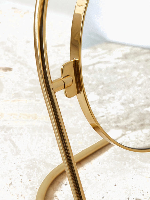 A detailed close-up of the Nimbus Table Mirror, showing the polished brass hinge connecting the circular mirror to its stand.