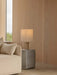 The lit Nonna Table Lamp on a grey Volume Side Table in a corner with wood-panelled walls and a cream sofa.