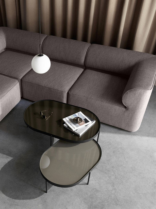 A modern living room with two glass NoNo Tables nested by a grey sofa, with a hanging lamp and taupe curtain.