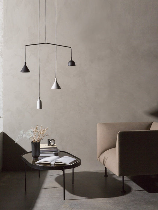 The black NoNo Table styled with books and a vase, next to a beige armchair. A contemporary pendant light hangs above.