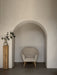 The Oda Lounge Chair, upholstered in a light fabric with wooden legs, sits inside an arched alcove next to a wooden plinth.