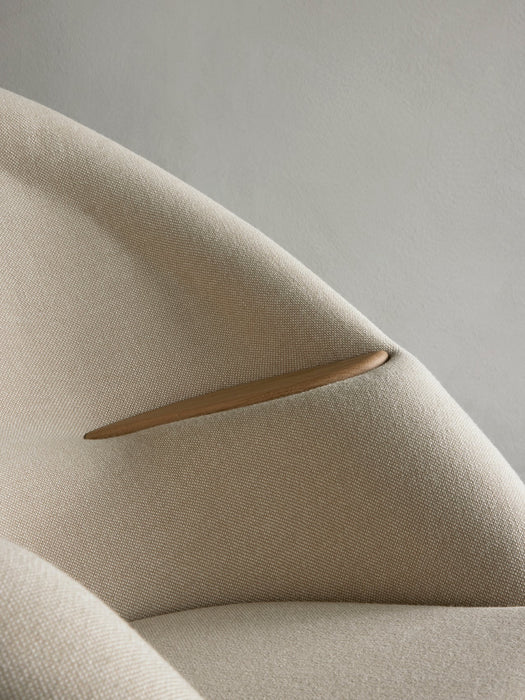 A close-up of the Oda Lounge Chair, showing the smooth wooden armrest seamlessly integrated into the light beige upholstery.