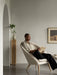 A man reads a book in the off-white Oda Lounge Chair. The room has grey walls, a wooden plinth, and an arched doorway.
